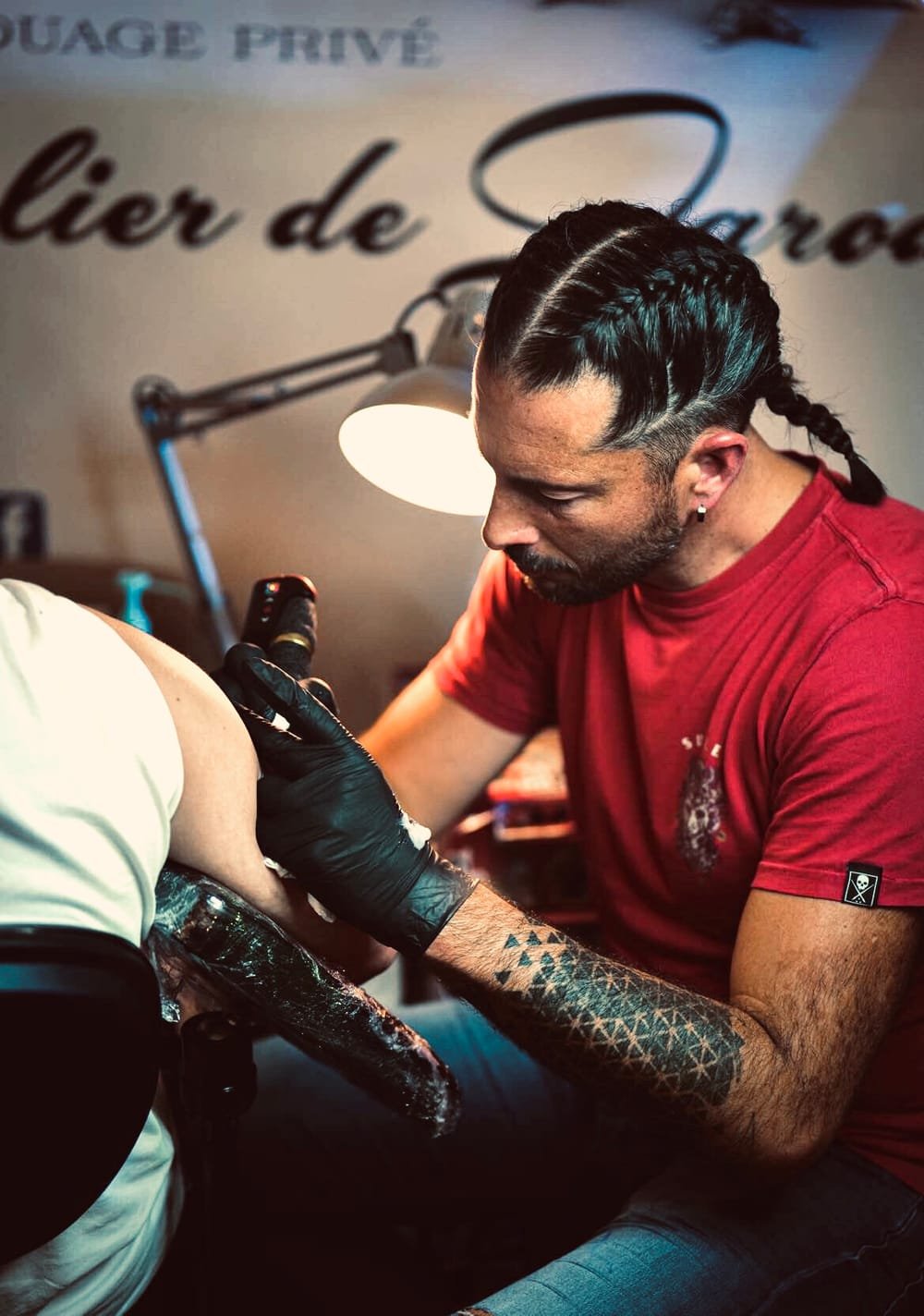 Jarod tatouant dans son atelier privé, l'enseigne « Atelier de Jarod » en arrière-plan