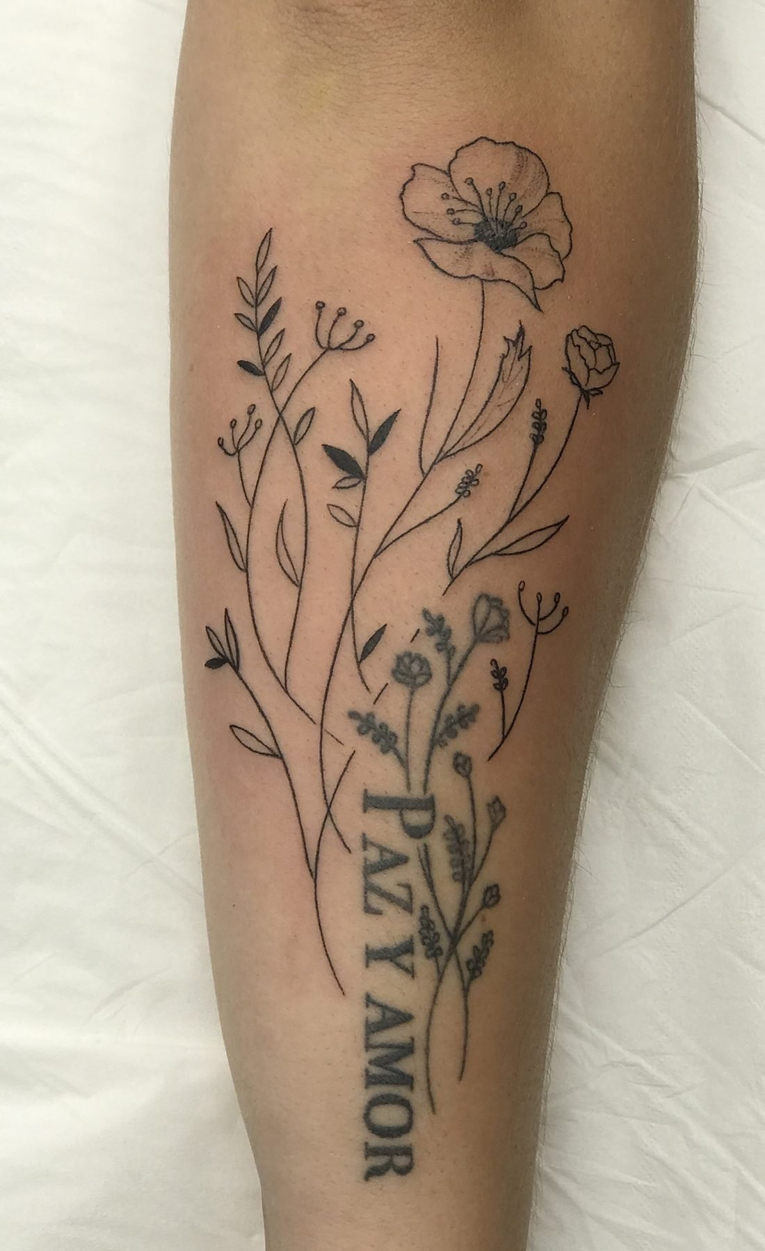 Tatouage floral en trait fin avec l’écriture Paz y Amor, sur l’avant-bras