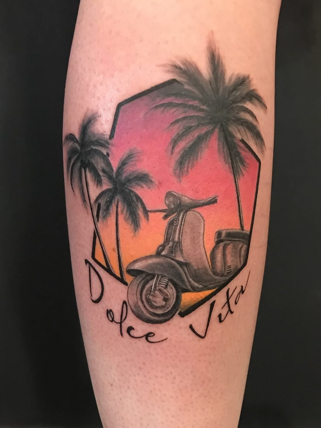 Tatouage en couleur : Vespa et palmiers devant un coucher de soleil, avec l’écriture Dolce Vita, sur le mollet