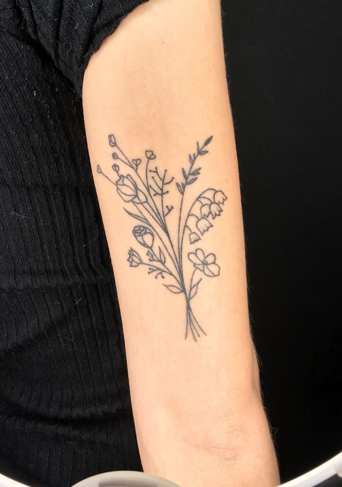 Tatouage fine line d’un bouquet de fleurs sauvages, à l’arrière du bras