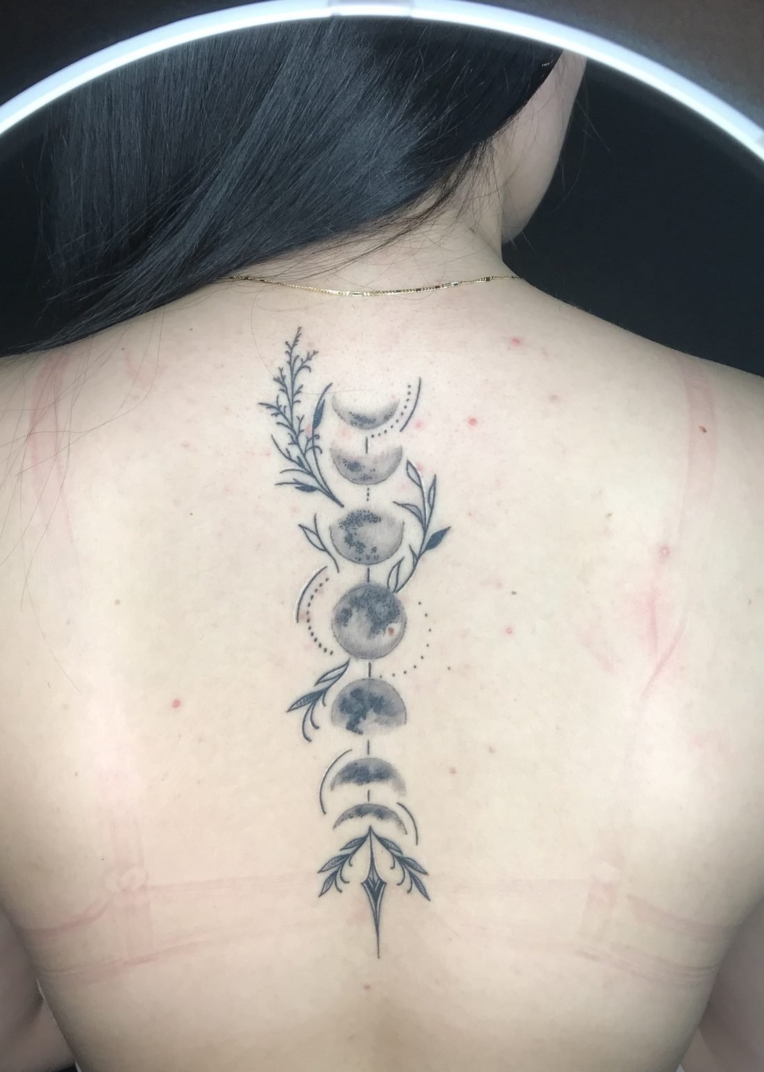 Tatouage fine line des phases de la lune et feuillages le long de la colonne vertébrale