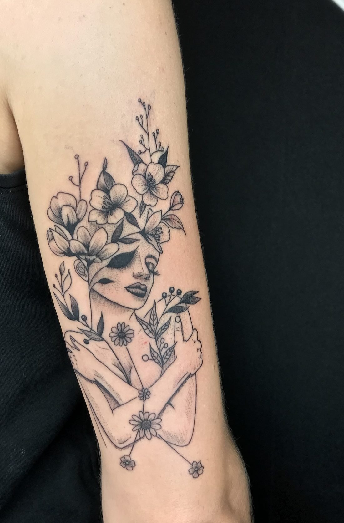 Tatouage floral en pointillé : femme qui s’enlace, la tête couronnée de fleurs, à l’arrière du bras